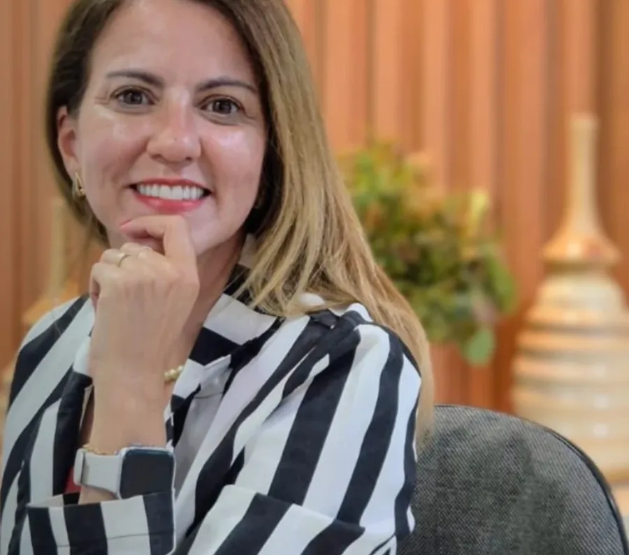 Dra. Júnia Santos sorrindo, com a mão no queixo, de camisa listrada
